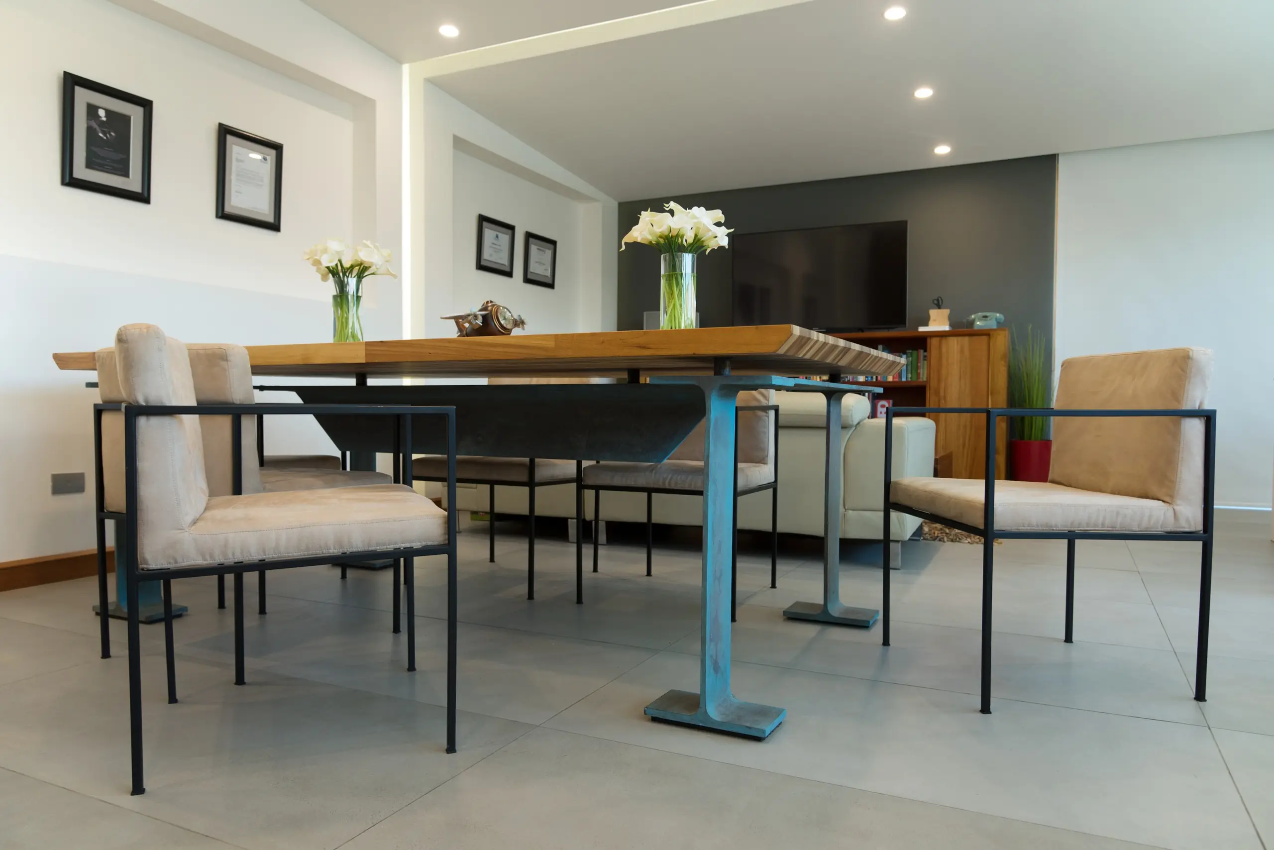 Mesa de reuniones de madera maciza con sillas tapizadas vacías y un florero de calas, en la oficina del estudio