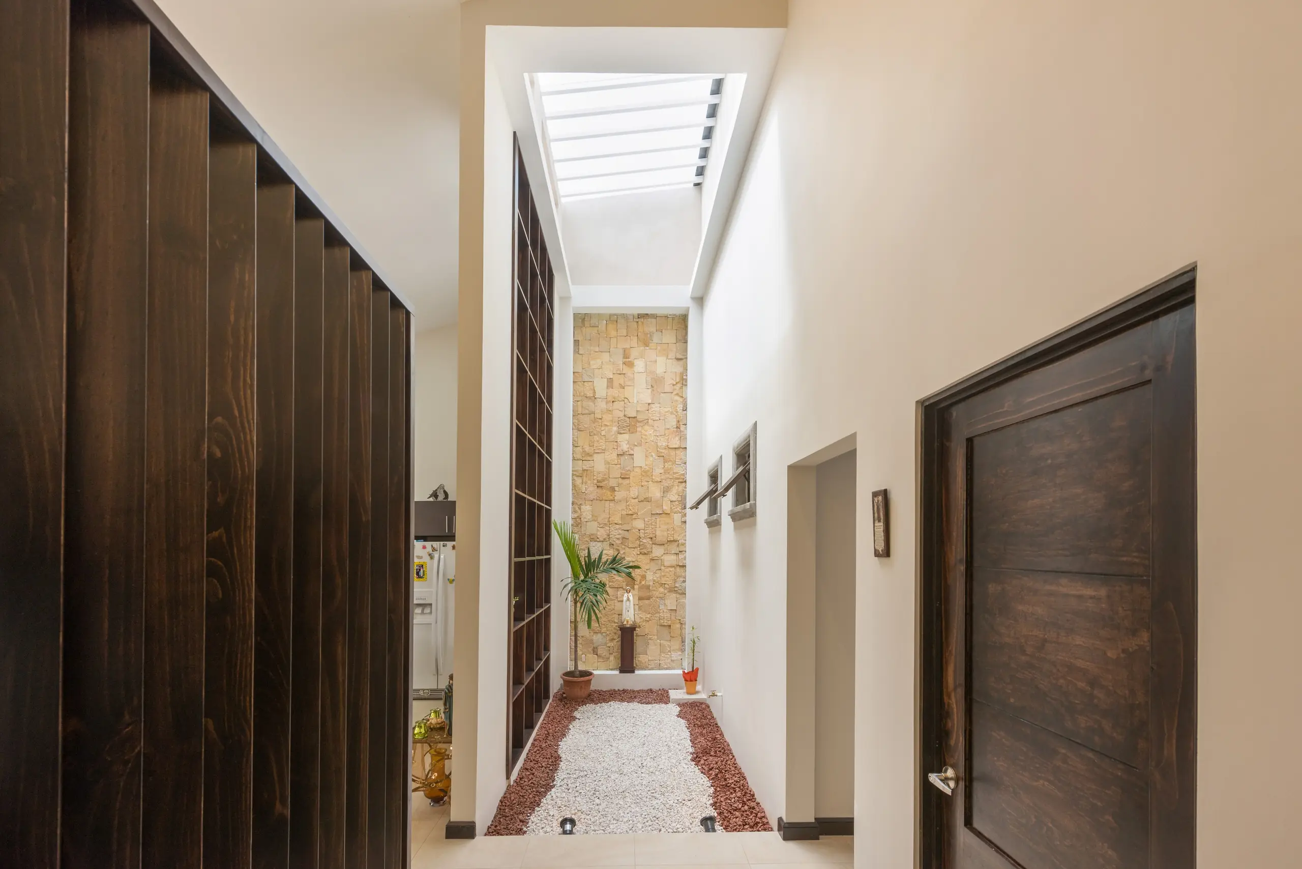 Vestíbulo con divisiones de madera oscura que se abre a un patio interior de piedra bajo una luz cenital