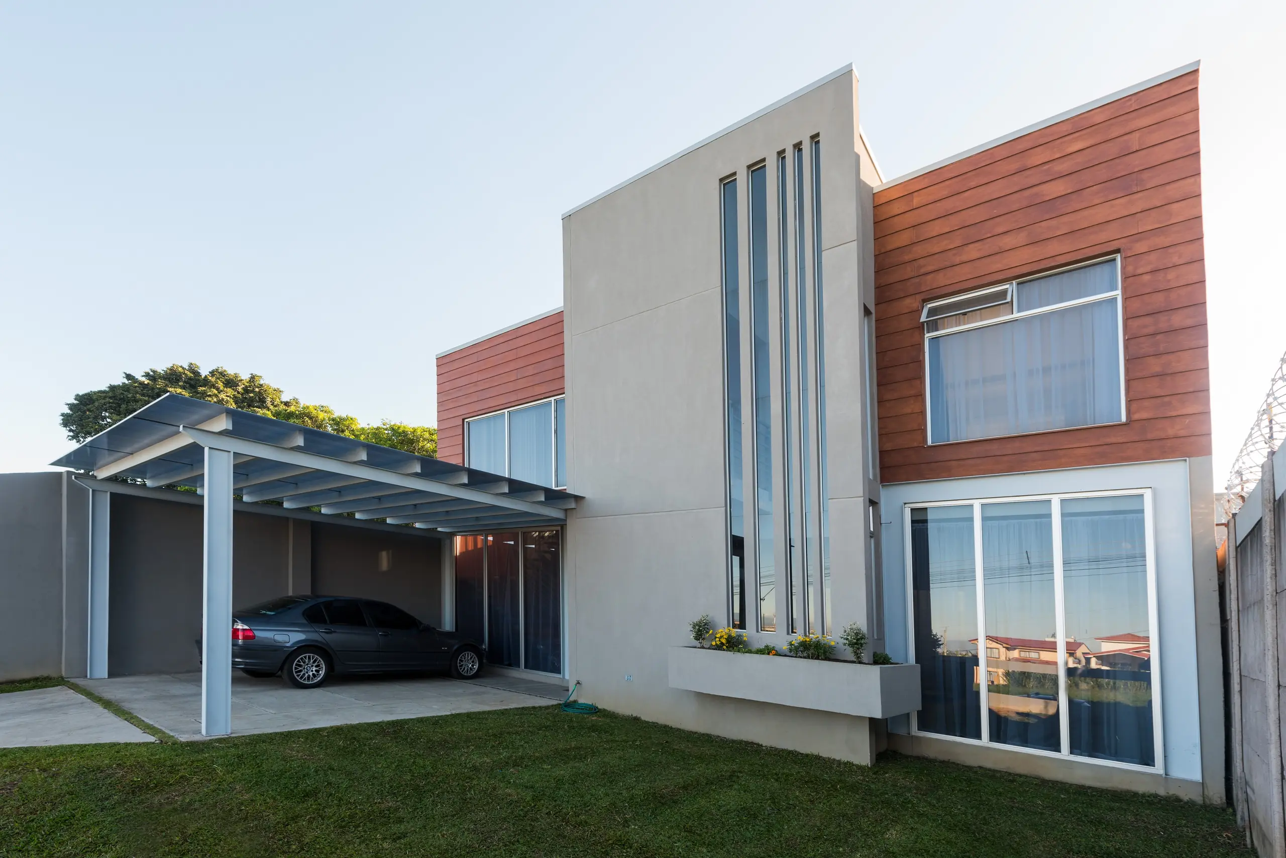 Casa de dos niveles con revestimiento de madera, ventanal vertical de piso a techo y cochera de estructura liviana